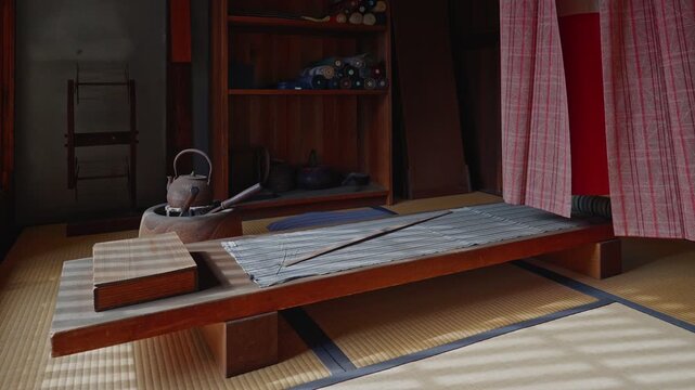 An interior view of a historic Japanese workroom featuring a wooden kimono hanger (Ikou) and textile rolls. Soft sunlight filters through shoji screens, illuminating the tatami floor and creating a se