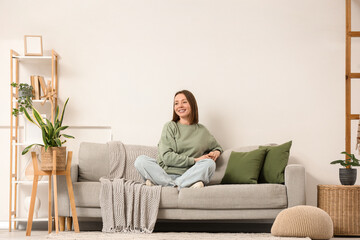 Happy young woman sitting on grey sofa in living room