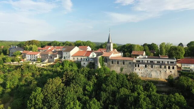 Scenic aerial view of the historic village of Hattonchatel with stone buildings, a church, and lush green surroundings under a clear sky.
