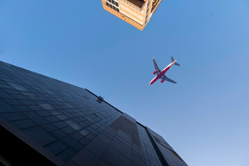 Airplane flying low over business skyscrapers building on blue sky