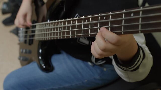 A detailed close-up video shows a child's hands playing an electric bass guitar. The focus is on the fretboard as their fingers press the strings, practicing a song.