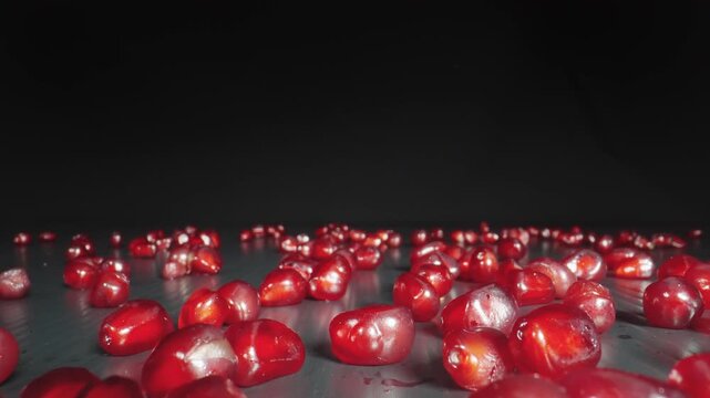Healthy pomegranate fruit grains spread on black board with dark background, macro dolly shot with probe lens