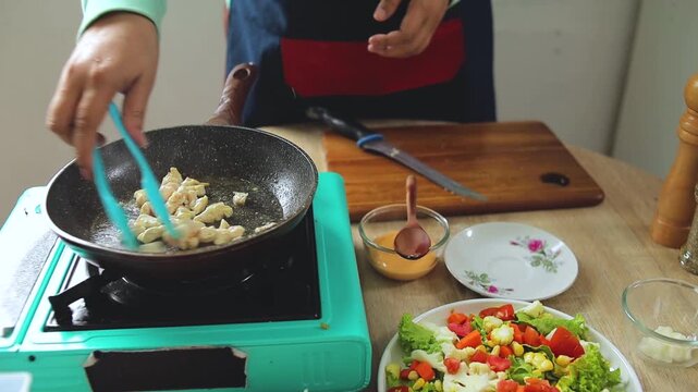 Chef Hands stir-frying bite-sized chicken pieces in pan for fresh salad