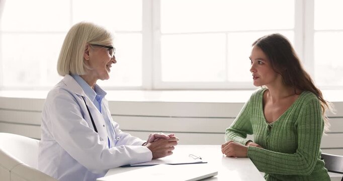Female doctor in white coat sits at desk and explains medical results to woman patient, clarifying diagnosis, treatment options during consultation in clinic office. Professional health care services