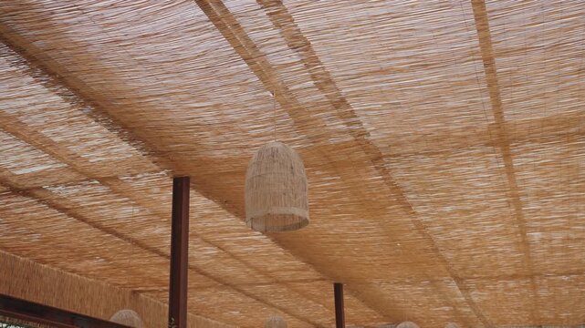 Upward view of woven straw ceiling canopy with suspended wicker lamp creating warm natural texture and soft light pattern