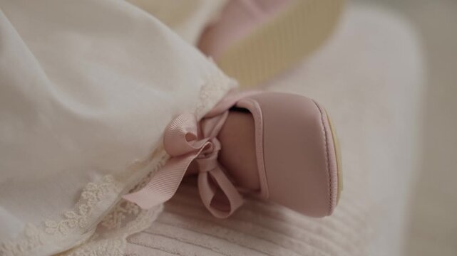 Close up of infant foot wearing soft pink shoe with ribbon tied over white lace baptism gown during christening ceremony
