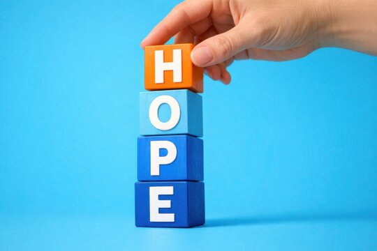 Beacon of Optimism: A person's hand meticulously positions a vibrant block, culminating in the word 'HOPE', against a backdrop, symbolizing enduring optimism and unwavering faith.