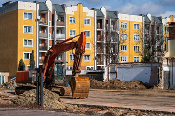 Orange crawler excavator on a cleared construction site next to a modern yellow apartment block, documenting urban revitalization, old building demolition, and site preparation for new infrastructure  © Adam