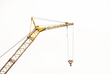 A professional yellow lattice boom crane with a steel hook suspended against a neutral bright background. This minimalist industrial shot emphasizes the power and scale of modern engineering machinery © Alina Ziabrieva