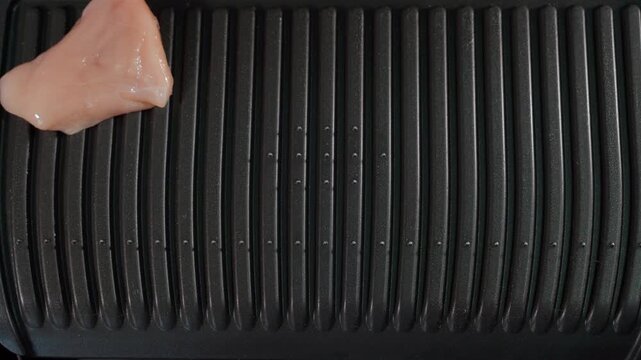 Top view of a chicken breast being placed on an electric grill with tongs