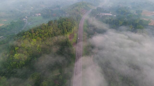 4K drone shot of a misty expressway surrounded by dense tropical nature illuminated by sunrise