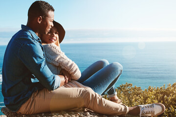 Couple, smile and hug with ocean view on holiday for bonding, relax or space at beach on mountain. Man, woman and talk with interracial relationship, embrace and connection at seaside on vacation