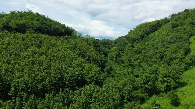 Lush green hills and scattered rural buildings under a cloudy sky in the countryside between Luang Prabang and Nong Khiaw, Laos.