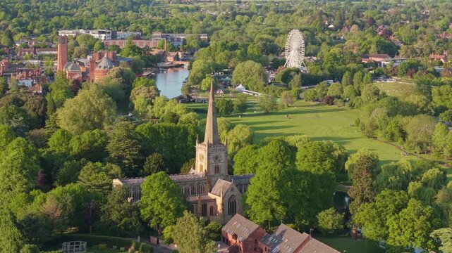 A drone orbit around the Gothic Holy Trinity Church, sweeping around the spire to reveal the winding River Avon and the historic Stratford-upon-Avon town center in the background.