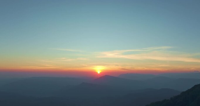 A breathtaking aerial view captures the golden sunrise rising above a vast canopy of pine trees and mist-covered mountains. Soft morning light paints the forest in warm hues, creating a peaceful