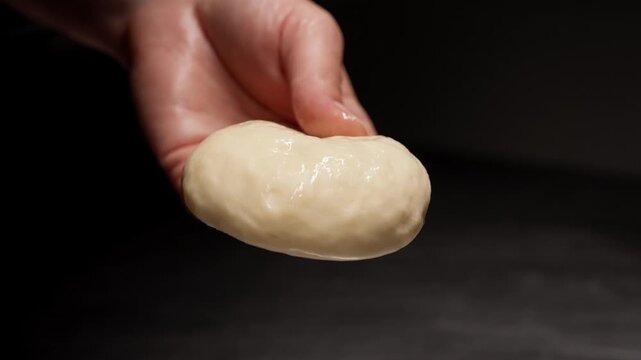 Close-up transformation of a smooth ball of raw dough being shaped and rested on a reflective metal surface in a minimal, softly lit kitchen setting