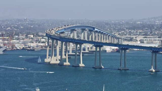Coronado bridge with boats crossing the bay in foreground, showing dynamic motion of vehicle traffic and marine activity, with city skyline in background