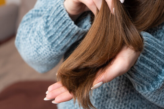 Woman showing split ends on dry winter hair in cozy sweater  
