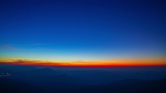 In a smooth flow of changing light, the sun emerges beyond towering peaks, transforming the sky into a glowing canvas. The time lapse reveals the tranquil charm of dawn across the vast mountain range.