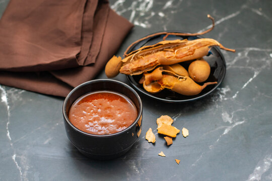 Tamarind sauce in white bowl with whole pods, spicy chutney dip, Indian cuisine ingredient, marble background, top view food photography
