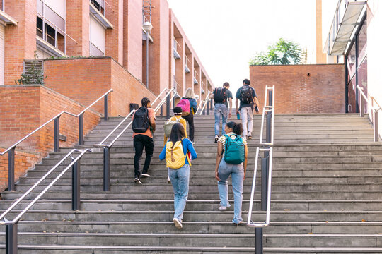 Group of diverse students with backpacks walking up outdoor stairs at a university campus, representing education and progress