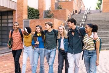 Obraz premium Group of diverse university students walking arm in arm, laughing and smiling on campus with backpacks and books