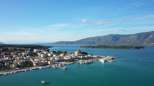 Scenic aerial view of the coastal village of Kilada, Greece, featuring a picturesque harbor, traditional houses, and calm blue waters under a clear sky.