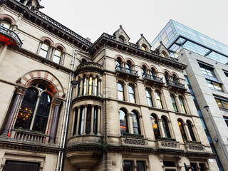 Historic Victorian facade in Manchester juxtaposed with modern glass building on a city street © AS Photo Family
