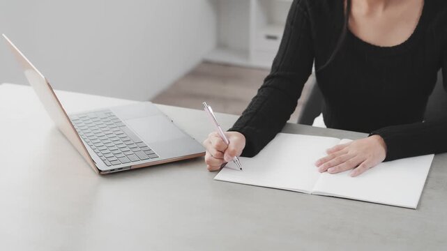 デスクでノートパソコンを見ながら勉強する女性