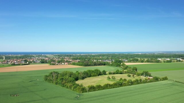Drone shot of lush green fields and rural landscape near Batteries Hillman in Normandy, France, with the coastline visible in the background under a clear blue sky.