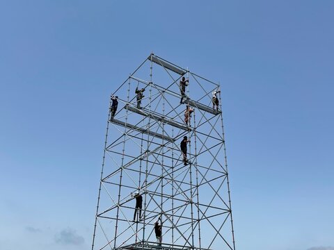 Construction workers on metal scaffolding working at height under a clear blue sky with copy space.