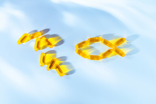 Golden omega 3 fish oil capsules arranged in the shape of a fish on blue background, symbolizing dietary supplements, vitamins and healthy nutrition for well being