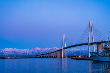 夕方の海王丸パークから新湊大橋と海王丸を前景にピンク色染まる立山連峰アーベンロート