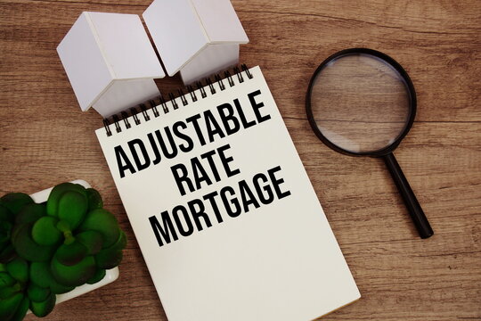 ARM Adjustable Rate Mortgage text written notepad with house model and magnifying glass on wooden background