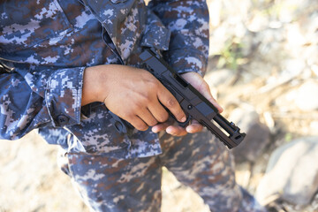 Obraz premium Focused soldier in blue camouflage uniform holding tactical handgun. Close up of military person hand preparing weapon for combat or law enforcement duty