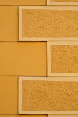 Fototapeta premium A close up of a yellow building facade featuring rectangular decorative elements with a rough mineral texture arranged in a staggered pattern