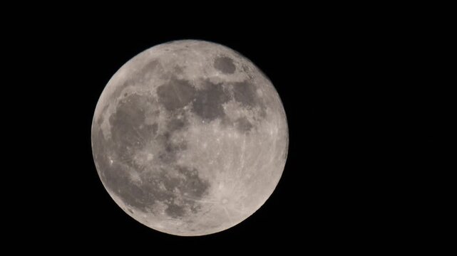 Full moon glowing in the night sky. Detailed lunar surface visible with craters and texture. Bright full moon isolated against a dark black background. Astronomy, space, nature and night concept.