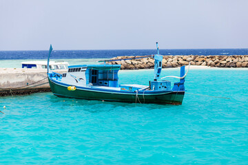 Obraz premium Bright blue boat rests near rocky breakwater