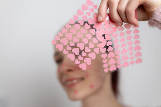 Hand holding colorful heart shaped acne patches for skincare treatment. Beauty routine concept with cosmetic pimple stickers for facial care.
