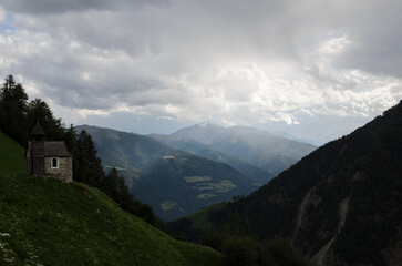 Small stone chapel on a mountain slope under dramatic sky