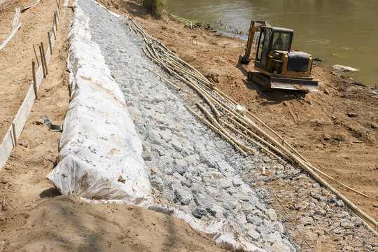 Riverbank stabilization work with geotextile fabric and riprap rock. construction site shows erosion control and civil engineering with bulldozer on an earth bank for infrastructure