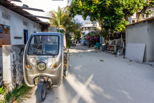 Silver auto-rickshaw parked beside a worn wall