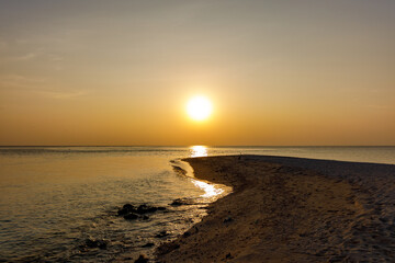 Obraz premium Golden sun dips low over calm ocean waters