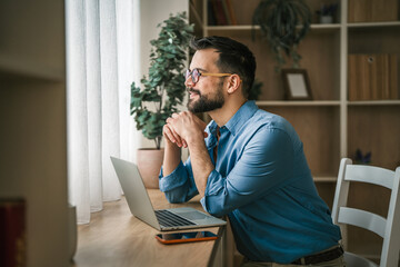 Naklejka premium Man thinking while working in home office with laptop