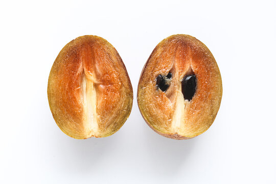 Top view of a single sapodilla (sawo manila) fruit sliced in half, revealing its rich, caramel-colored flesh.