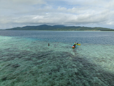 Aerial view of people canoeing in turquoise waters meeting the horizon, revealing a lush green mountain landscape in the distance, Karimunjawa, Central Java, Indonesia