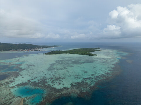 Aerial view of an island surrounded by turquoise waters meeting the deep blue sea under a vast sky at Menjangan Besar Island, Karimunjawa, Central Java, Indonesia.