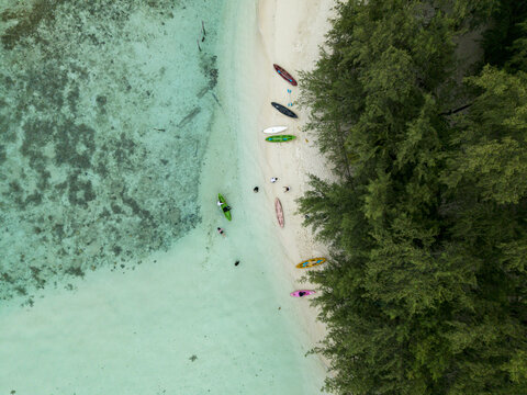 Aerial view of turquoise waters meet the shore, where colorful kayaks rest beside the lush green trees of Menjangan Kecil Island, Karimunjawa, Central Java, Indonesia.