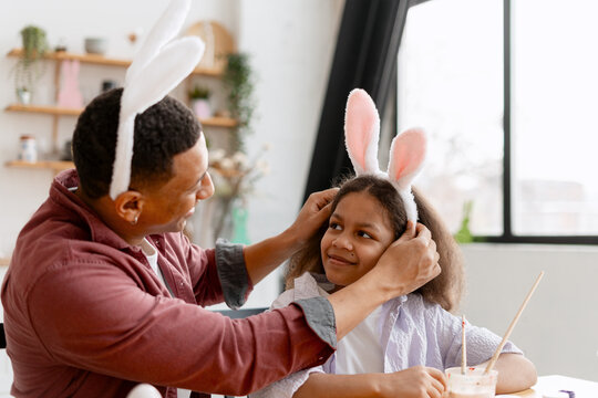 Father placing bunny ears on his smiling daughter during an Easter celebration