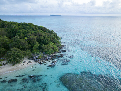 Aerial view of turquoise waters meeting the lush green coastline at Tanjung Gelam Beach, a tropical haven, Karimunjawa, Central Java, Indonesia.